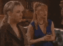 two women are sitting next to each other on a couch talking to each other .