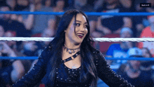 a woman in a black jacket is standing in a wrestling ring and smiling .