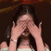 a woman covering her face with her hands and a necklace that says ' a ' on it