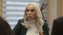 a woman with blonde hair is wearing a green jacket and a white turtleneck
