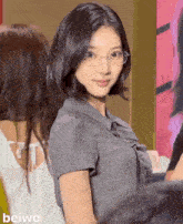 a girl wearing glasses and a gray shirt with the word beiwo on the bottom left