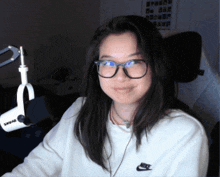 a woman wearing glasses and a nike sweatshirt stands in front of a shure microphone
