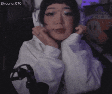 a woman is sitting in front of a microphone wearing a white hoodie with cat ears .