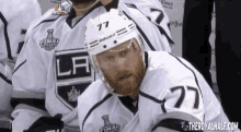 a hockey player with the number 77 on his helmet sits in the dugout