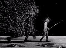 a black and white photo of a man holding a stick in front of a large monster