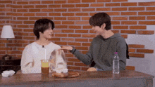 two men are sitting at a table with a bottle of water and a cup of orange juice .
