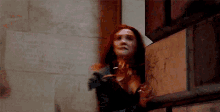 a woman with red hair is standing in front of a wooden wall .