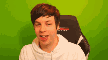 a young man is sitting in a racing chair with a green screen behind him