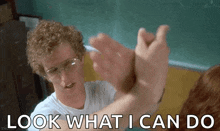 a man with curly hair and glasses is giving a high five to another man in a classroom .