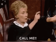 a judge is sitting at a table in a courtroom giving a thumbs up and telling someone to call her .