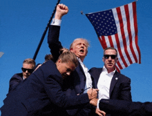 a man in a suit holds up his fist in the air in front of a flag
