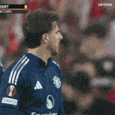 a man wearing a blue adidas jersey stands in front of a crowd