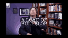 a man in a suit is sitting in front of a bookshelf with the words a load of bullplop above him