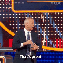 a man in a suit and tie is standing on a stage holding a trophy and saying that 's great .