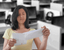 a woman in a yellow shirt is holding an envelope with a letter inside of it