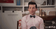 a man in a pink shirt and bow tie is sitting in front of a netflix sign