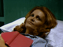 a woman with red hair is laying in a hospital bed holding a book