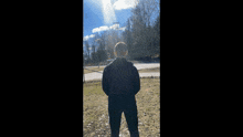 a man in a black jacket is standing in a field looking at the sky