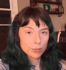 a woman with green hair is taking a selfie in front of a mirror .