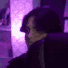 a close up of a person 's face in a dark room with purple lights behind them .