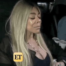 a woman with blonde hair is sitting in a car with her eyes closed and a yellow icon that says et on it .