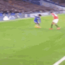 a soccer player in a blue jersey is running on the field while another player in a red shirt is laying on the ground .