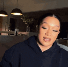 a woman wearing a black hoodie looks at the camera with her eyes closed