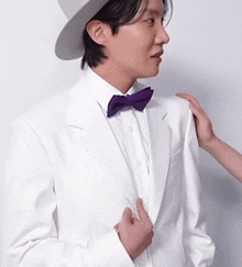 a man in a white suit with a purple bow tie and hat