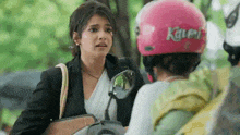 a woman wearing a pink helmet is talking to another woman while riding a motorcycle .