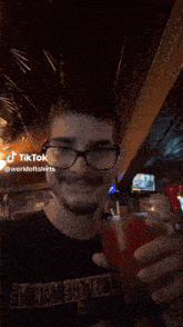 a man wearing glasses is holding a glass of red liquid with a straw and a tiktok watermark