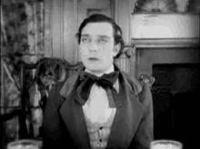 a man in a tuxedo and bow tie is sitting in a chair .