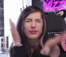 a woman is making a funny face with her eyes closed and her hands in the air .