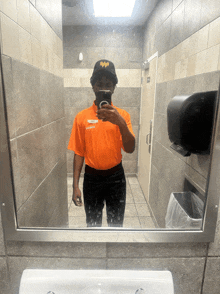 a man in an orange shirt taking a selfie in a bathroom mirror
