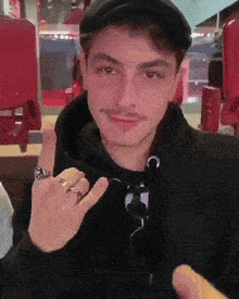 a man wearing a black hat and a black hoodie is making a devil horn sign