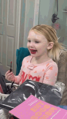 a little girl with red lipstick on her lips is holding a lipstick in her hand