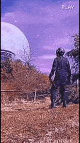 a man in a helmet is standing in a field looking at an alien flying in the sky .
