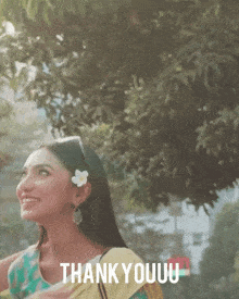 a woman with a flower in her hair is standing in front of a tree and says thank youuu