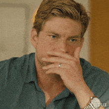 a man wearing a watch and a ring covering his mouth with his hand