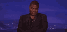 a man in a suit is standing on a stage with his hands folded in front of a blue background .