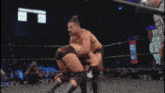 a referee watches two men wrestle in a ring and one of the men has the word slam on his shorts