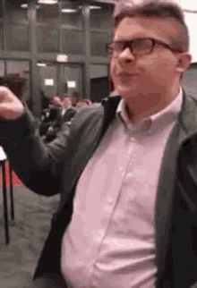 a man wearing glasses and a pink shirt is standing in a room with his arms outstretched .