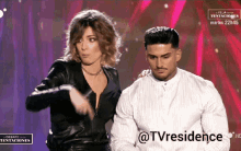 a woman in a black leather jacket is standing next to a man in a white shirt on a tv screen that says @tvresidence