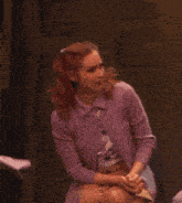 a woman in a purple sweater sits in front of a sign that says ' a ' on it