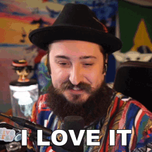 a man with a beard wearing a hat says " i love it " in front of a microphone