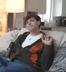 a man sitting on a couch holding a microphone and wearing a north face jacket