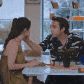 a man and a woman are sitting at a table with a plant in a pot .