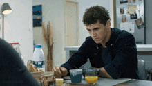 a man sits at a table with a glass of orange juice and a bottle of milk