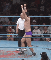 a wrestler in purple shorts stands in a ring with his fist in the air