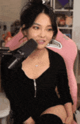 a woman in a black dress is sitting in front of a pink chair and talking into a microphone .