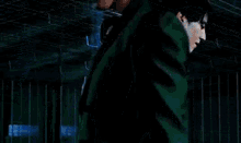 a man in a blue suit is standing in front of a fence in a dark room .
